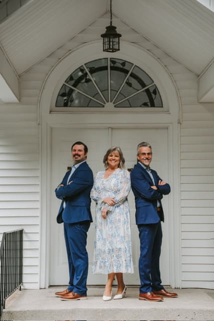 Mike, Chris, and Cathy Torrence standing together in front of a white chapel's arched doorway