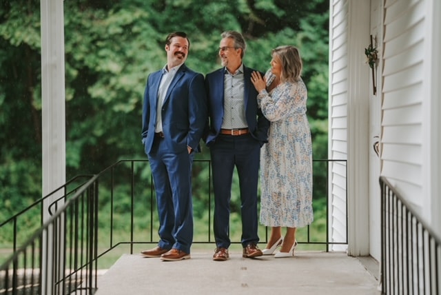 Mike, Chris, and Cathy Torrence on a church porch surrounded by green trees